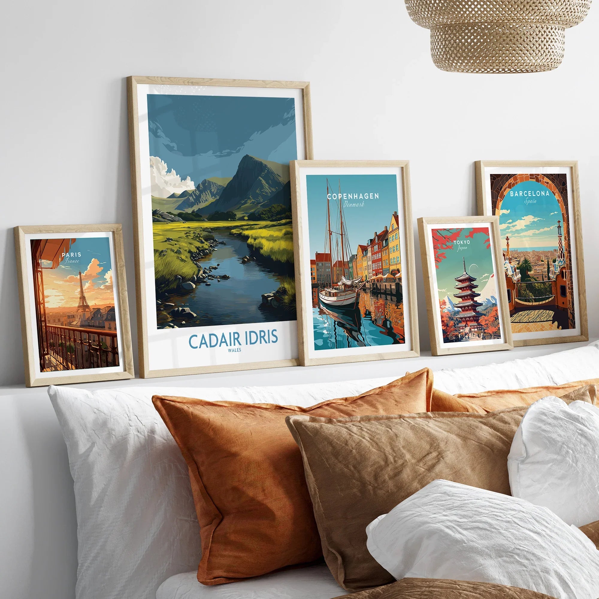 Set of five framed travel art prints above bed, featuring Paris, Cadair Idris, Copenhagen, Tokyo, Barcelona.