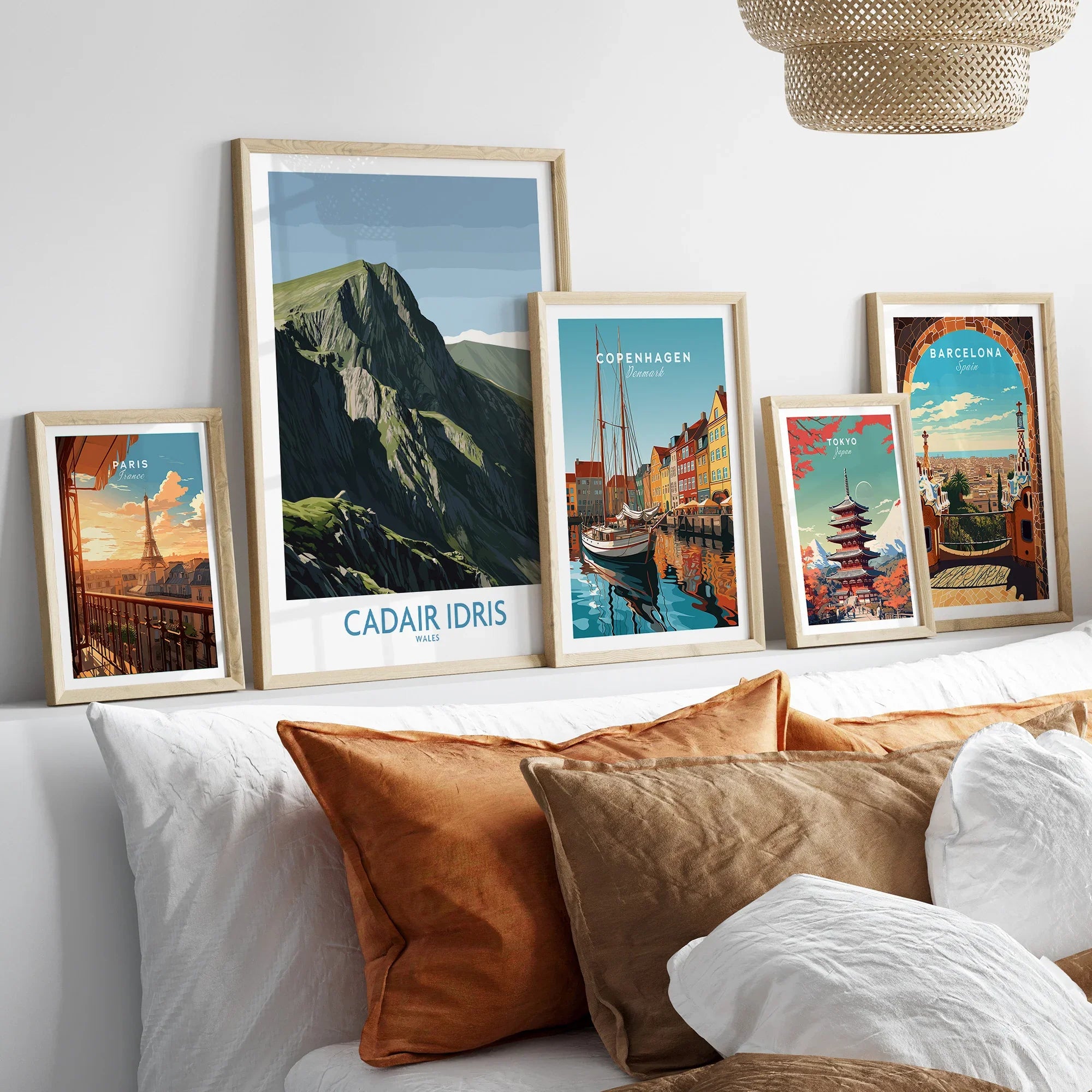 Five framed travel posters including mountains, city skylines, above a bed with earth-tone pillows.