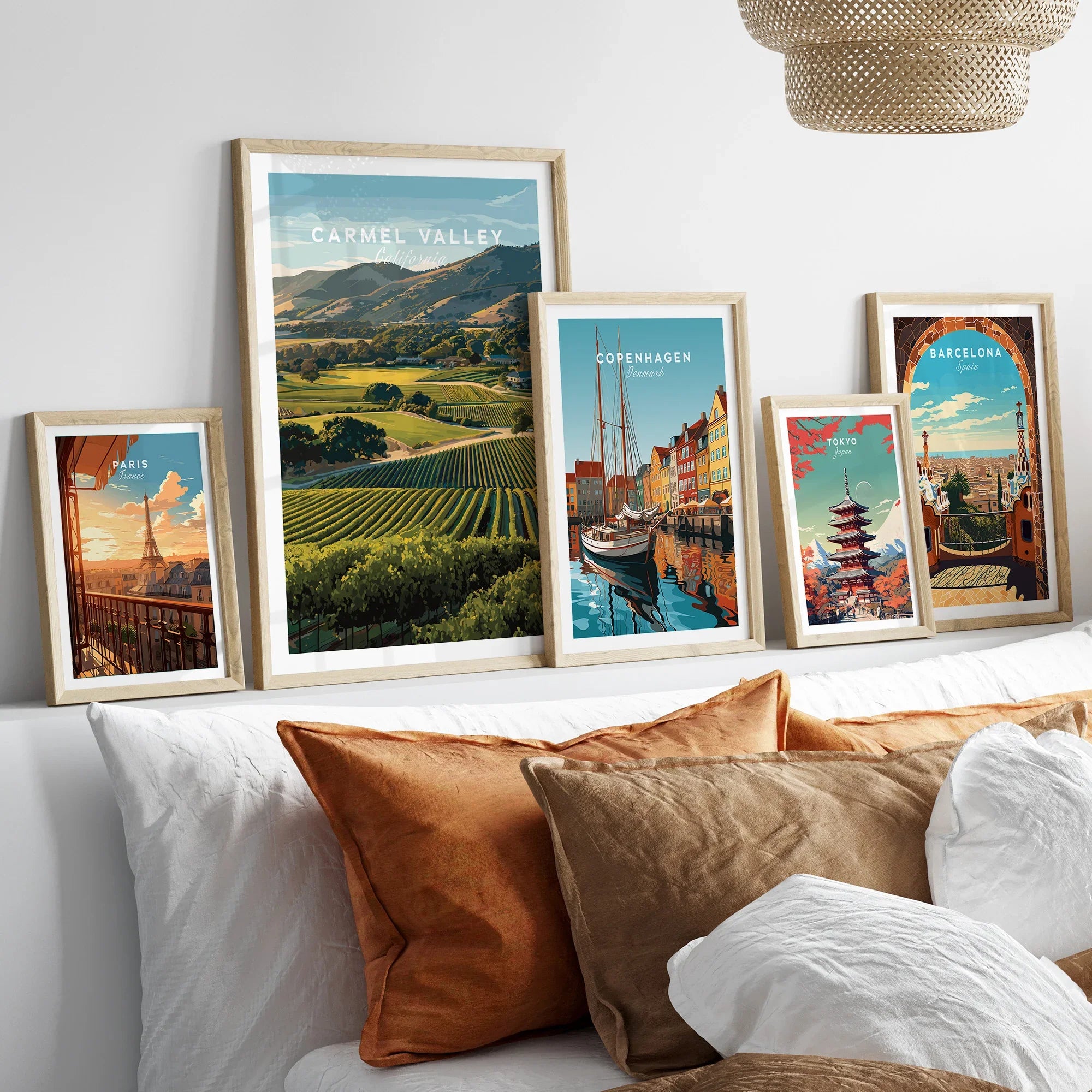 Five framed travel art prints featuring Carmel Valley, Paris, Copenhagen, Tokyo, and Barcelona above a bed with earth-tone pillows