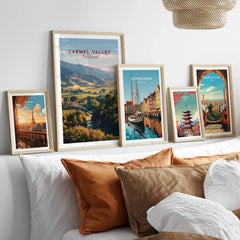 Set of five framed travel posters above bed, featuring Paris, Carmel Valley, Copenhagen, Tokyo, and Barcelona wall art prints in natural wood frames.