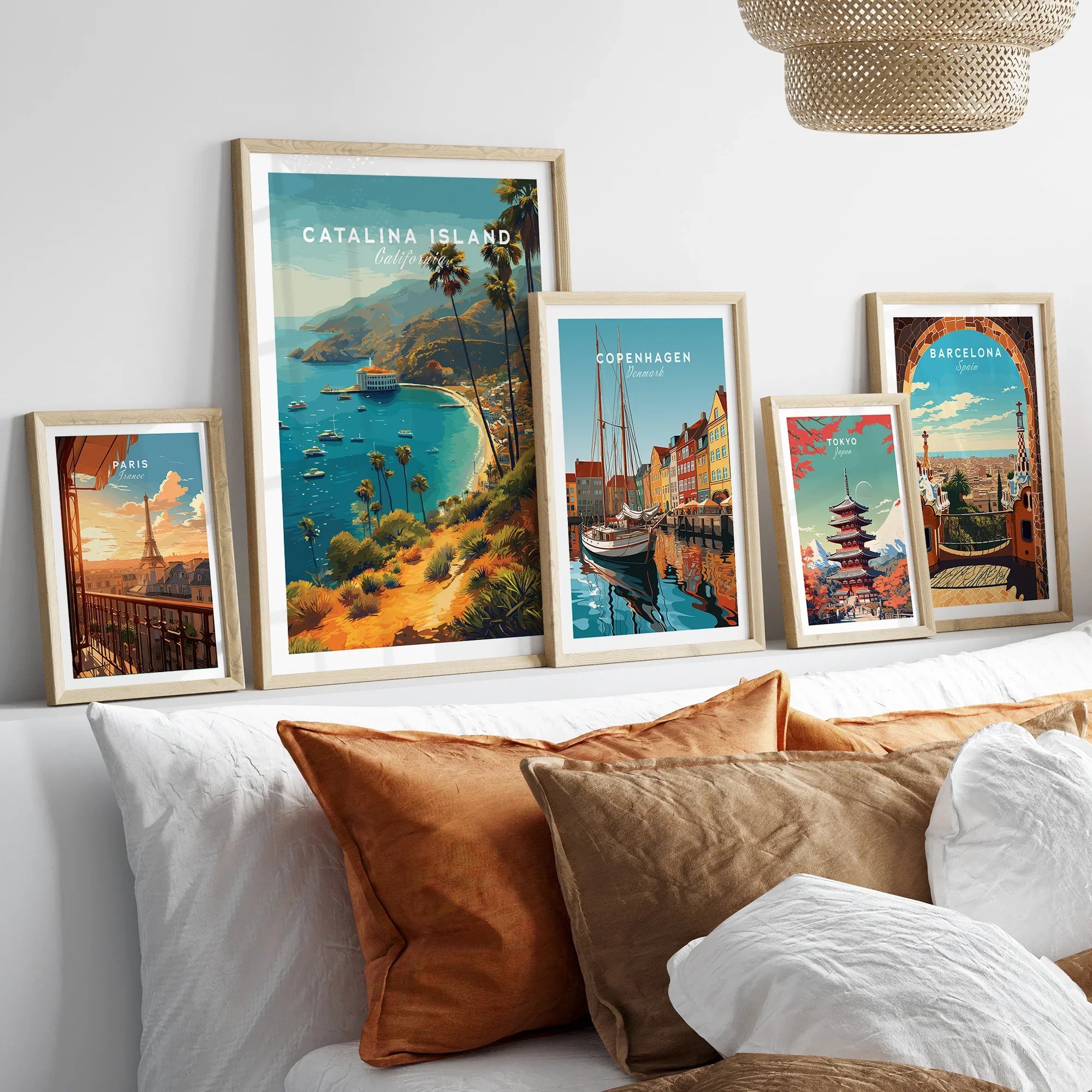 Set of five framed travel posters above bed, featuring Catalina Island, Paris, Copenhagen, Tokyo, Barcelona with natural wood frames.
