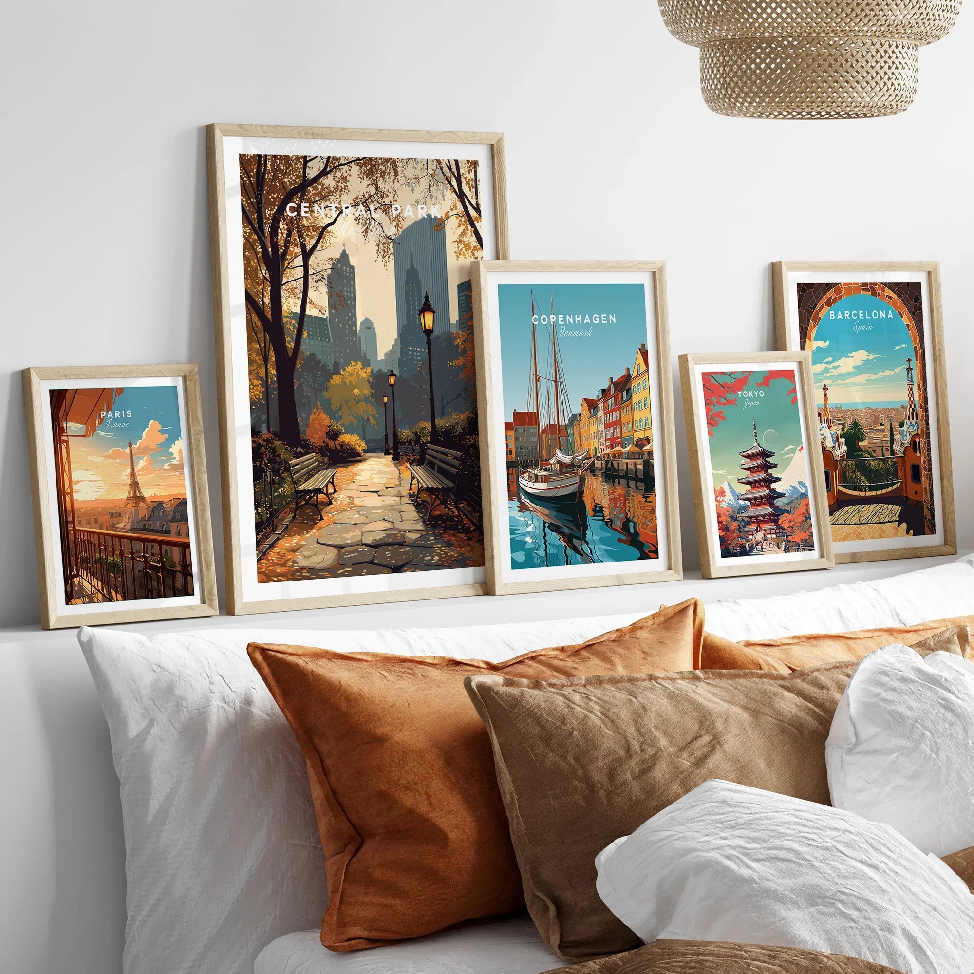 Five framed travel art prints above a bed, featuring landmarks from Paris, Central Park, Copenhagen, Tokyo, and Barcelona.