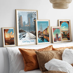 Travel city art prints in natural wood frames above a bed, featuring Central Park, Paris, Copenhagen, Tokyo, and Barcelona.
