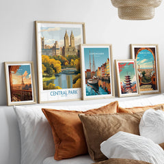 Travel posters art prints in natural wood frames above a modern bed, featuring Central Park, Paris, Copenhagen, Tokyo, Barcelona.