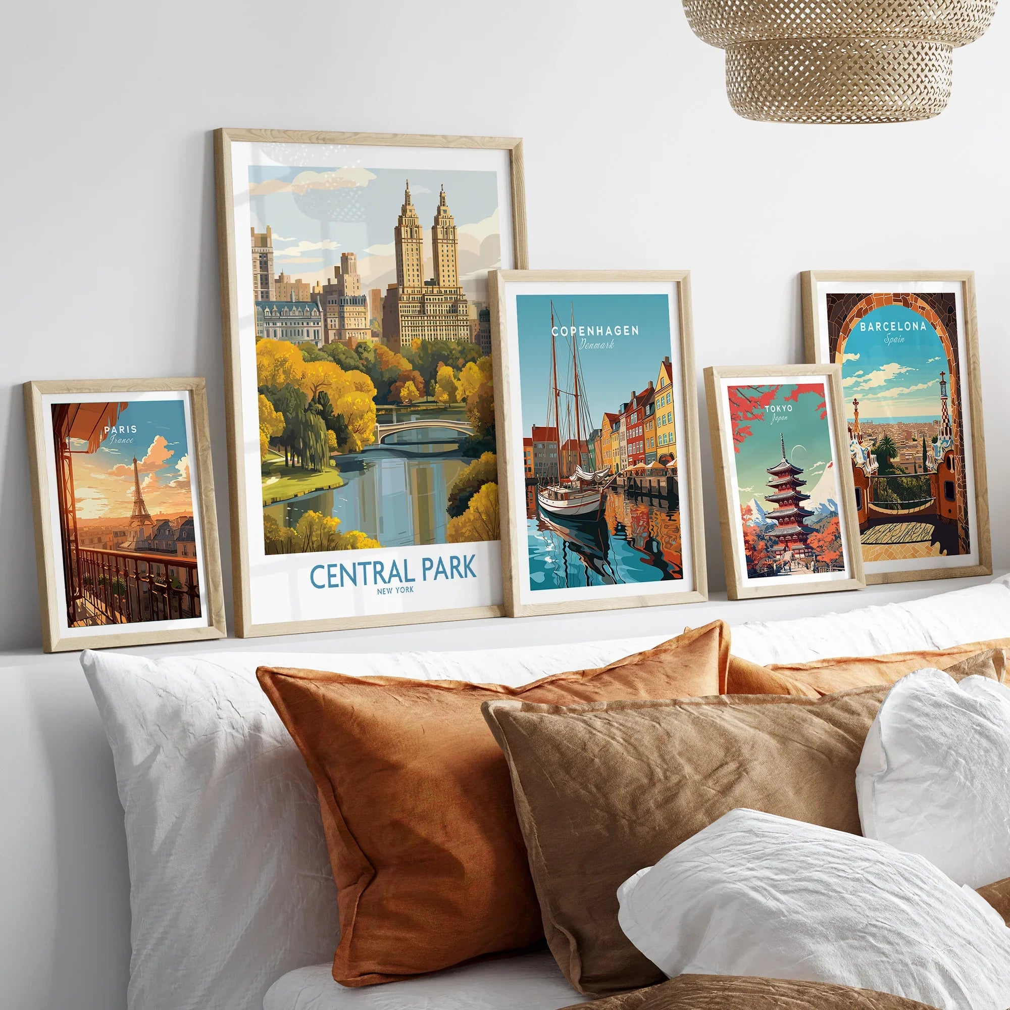 Travel posters art prints in natural wood frames above a modern bed, featuring Central Park, Paris, Copenhagen, Tokyo, Barcelona.