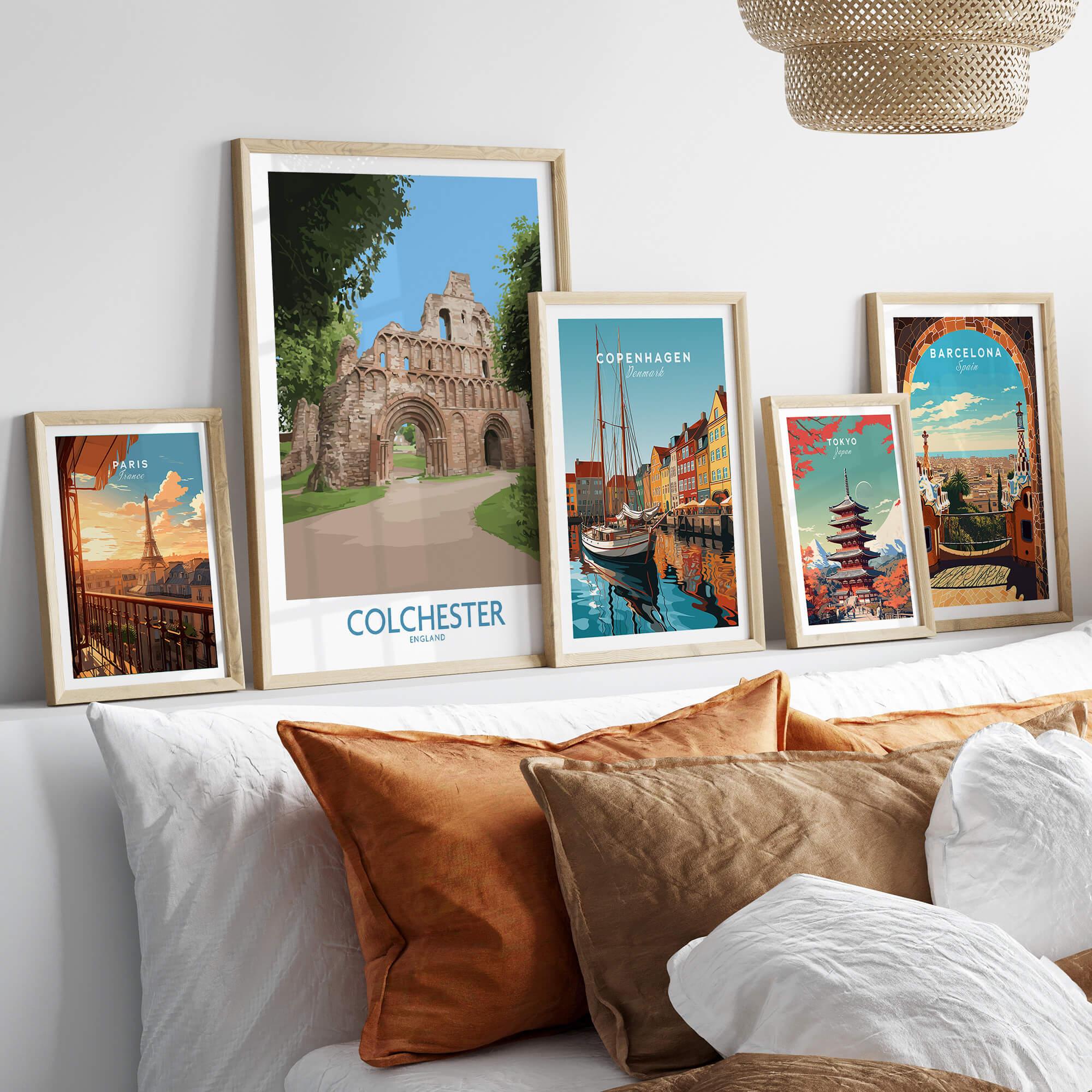 Set of five framed travel art prints above a bed, featuring Paris, Colchester, Copenhagen, Tokyo, and Barcelona landmarks in natural wood frames.
