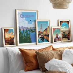 Set of five framed travel posters featuring Crater Lake, Paris, Copenhagen, Tokyo, and Barcelona above a bed with neutral decor.