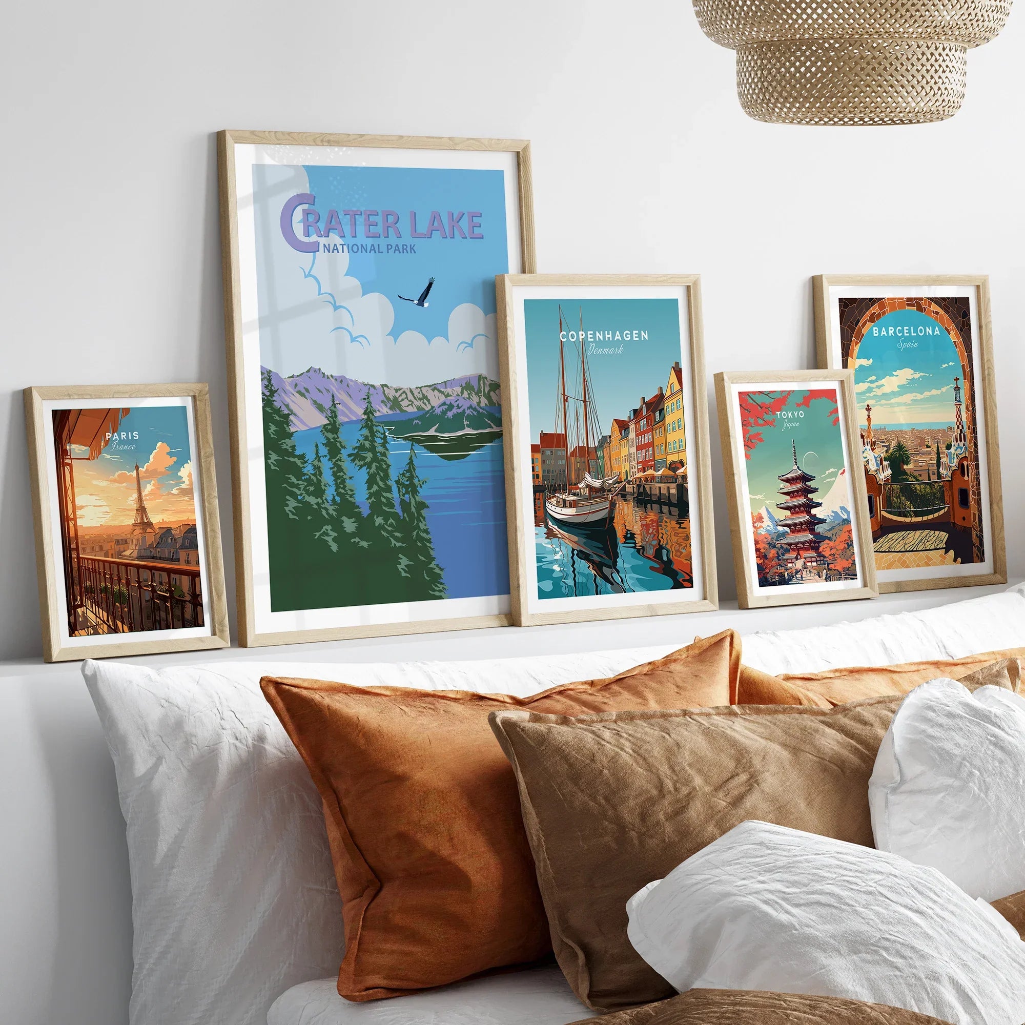 Set of five framed travel posters featuring Crater Lake, Paris, Copenhagen, Tokyo, and Barcelona above a bed with neutral decor.