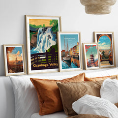 Five framed travel art prints above a bed, featuring Cuyahoga Valley, Paris, Copenhagen, Tokyo, and Barcelona.