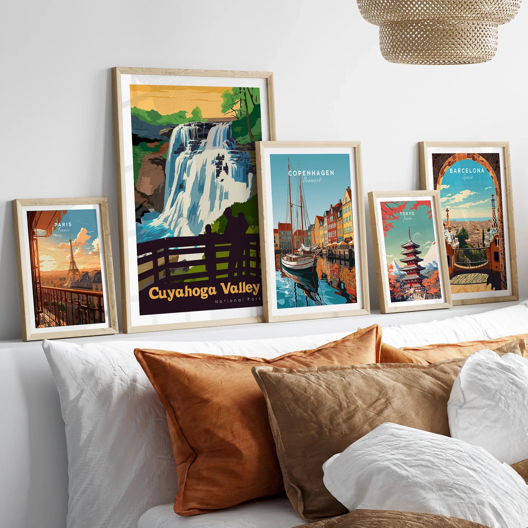 Five framed travel art prints above a bed, featuring Cuyahoga Valley, Paris, Copenhagen, Tokyo, and Barcelona.