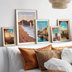 Durdle Door Travel Poster – Jurassic Coast Sunset Art displayed among other travel posters on a cozy sofa.