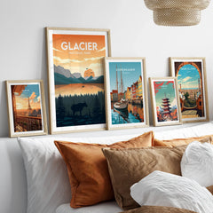 Set of five framed travel posters above bed, featuring Glacier National Park, Paris, Copenhagen, Tokyo, and Barcelona.