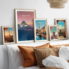 Travel art prints in natural wood frames above a bed, featuring Paris, Glacier National Park, Copenhagen, Tokyo, and Barcelona.