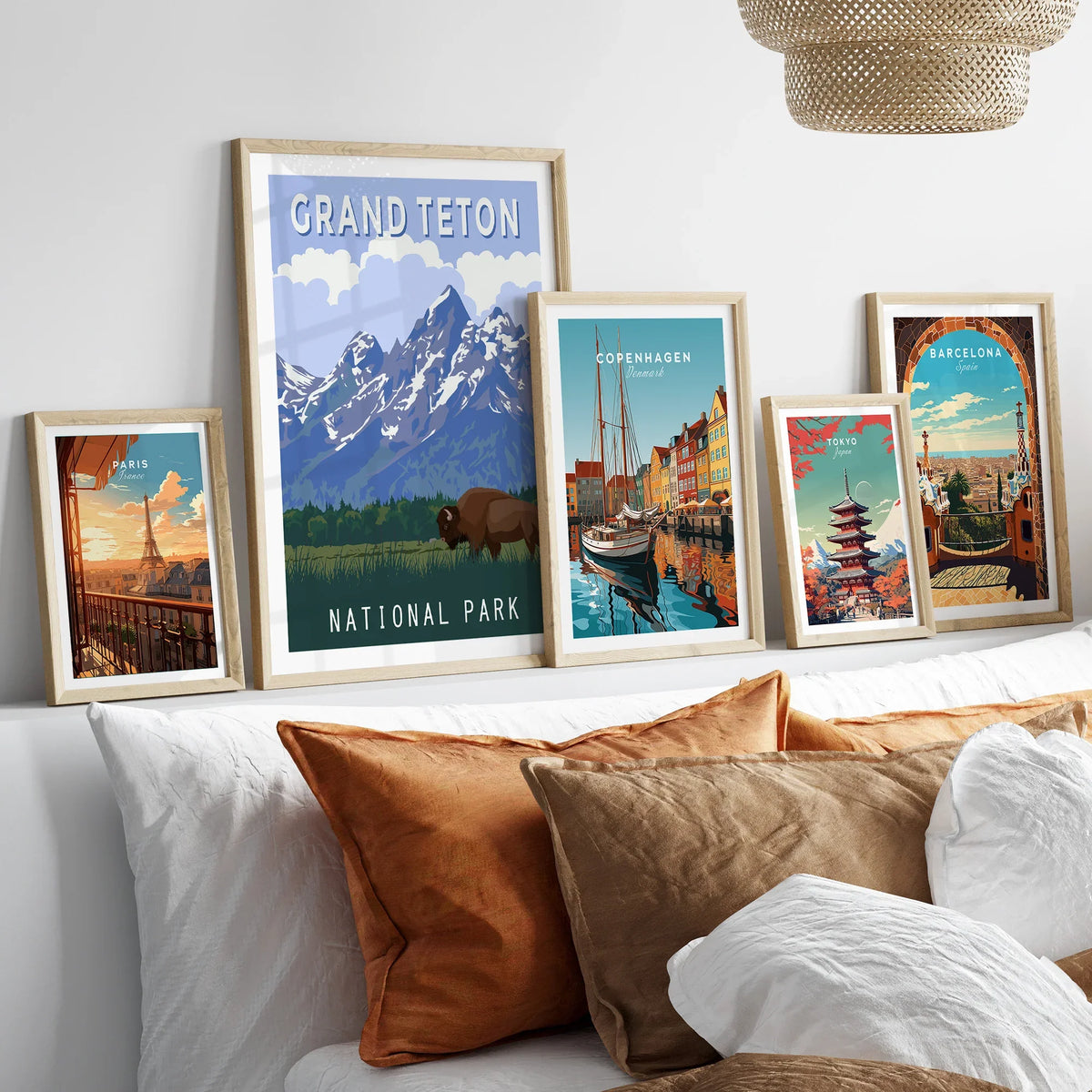 Set of five travel posters with natural wood frames above bed, featuring Grand Teton, Paris, Copenhagen, Tokyo, and Barcelona wall art.