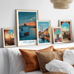 Holy Island Northumberland Poster | Coastal Castle Sunset Canvas Print displayed among other travel posters on a cozy sofa.