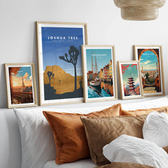 Framed travel poster prints of famous cities and Joshua Tree above a bed with cozy pillows
