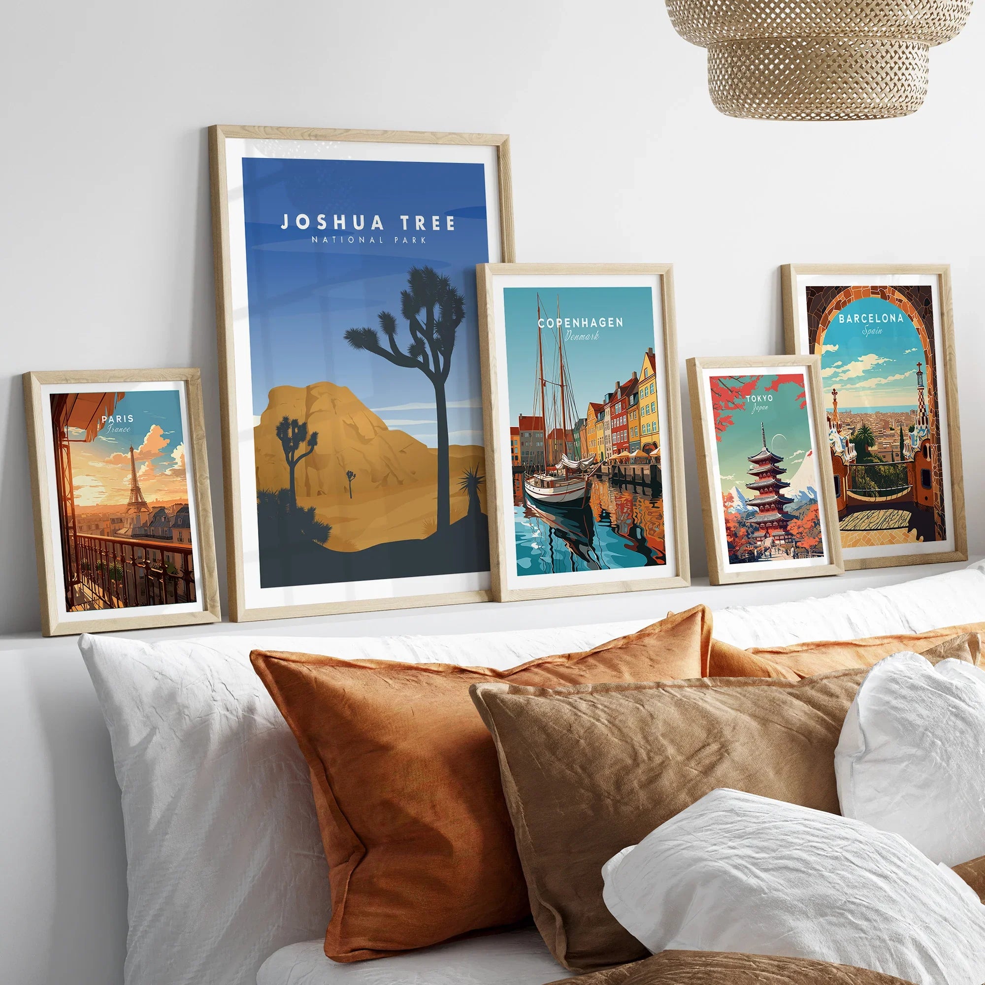 Framed travel poster prints of famous cities and Joshua Tree above a bed with cozy pillows
