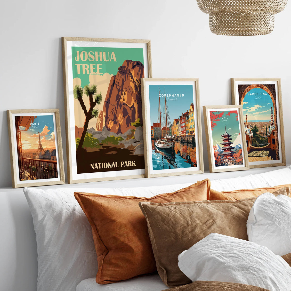 Gallery wall with framed travel posters of Joshua Tree, Paris, Copenhagen, Tokyo, and Barcelona above a bed.