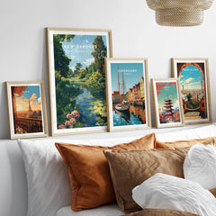 Set of five framed travel art prints featuring Paris, Kew Gardens, Copenhagen, Tokyo, and Barcelona above a modern bed with neutral pillows.
