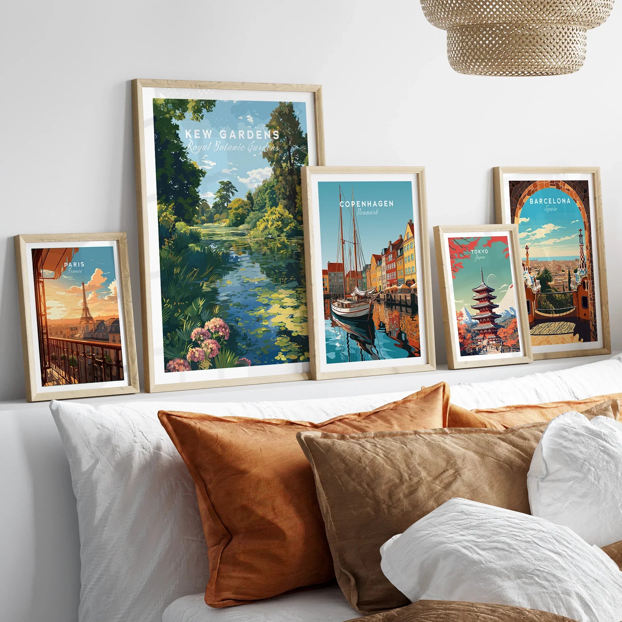 Set of five framed travel art prints featuring Paris, Kew Gardens, Copenhagen, Tokyo, and Barcelona above a modern bed with neutral pillows.