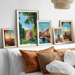 Framed travel posters of famous cities above a bed with neutral and orange pillows.