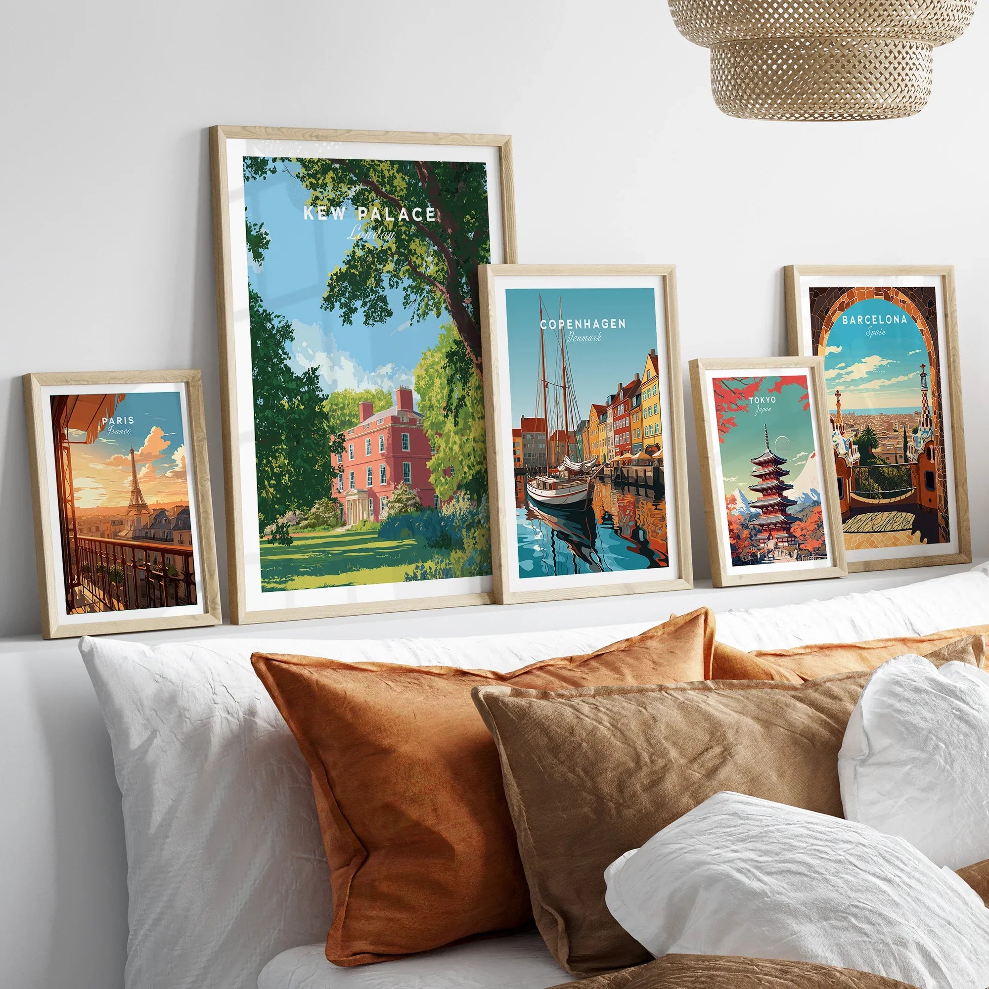 Framed travel posters of famous cities above a bed with neutral and orange pillows.