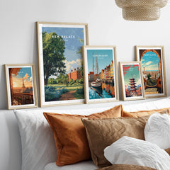 Set of five travel art prints in natural wood frames above a bed, featuring Paris, London, Copenhagen, Tokyo, and Barcelona landmarks.