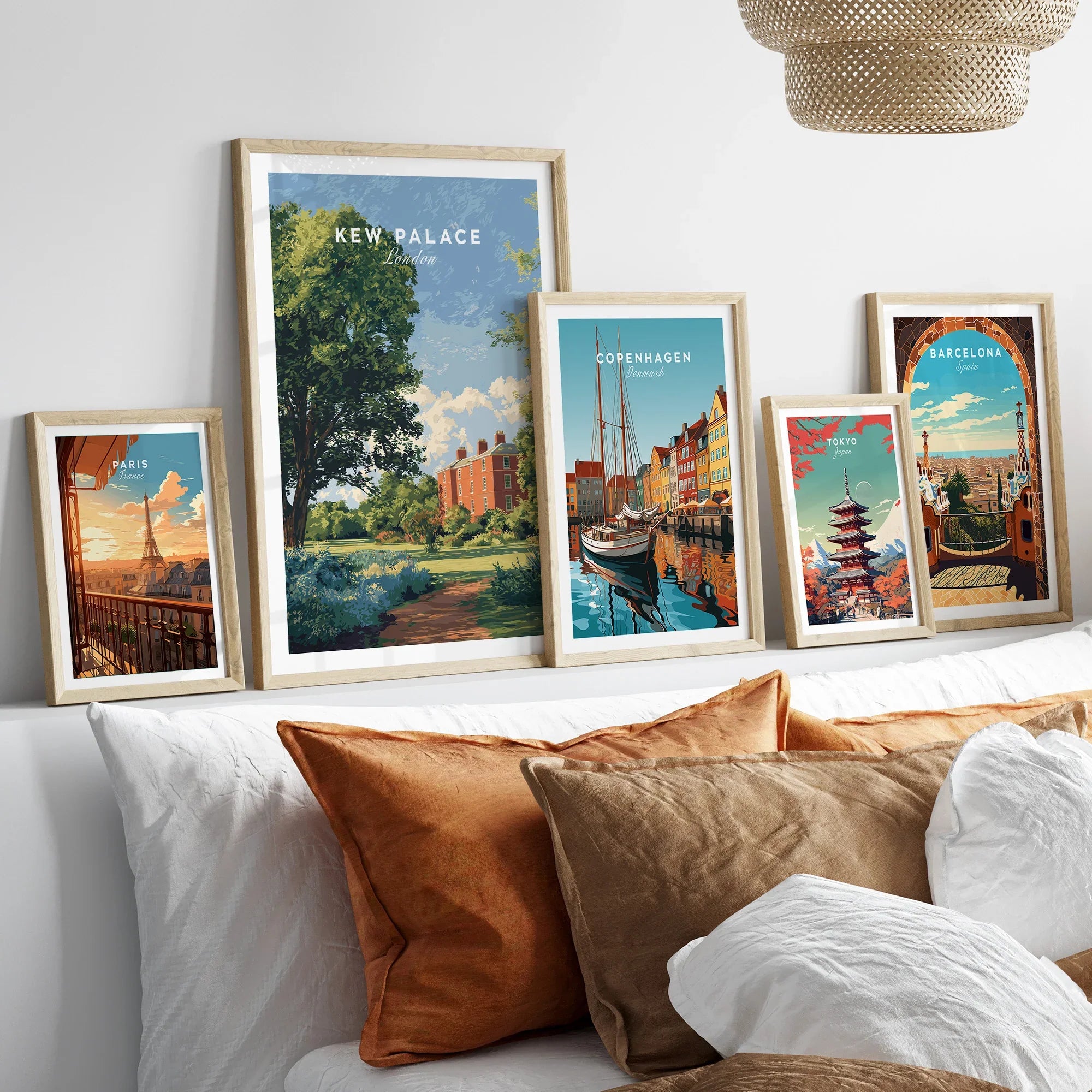 Set of five travel art prints in natural wood frames above a bed, featuring Paris, London, Copenhagen, Tokyo, and Barcelona landmarks.