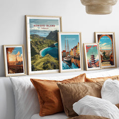 Five framed travel posters above a bed with natural wood frames and cozy pillows