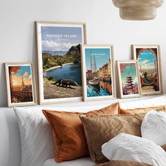 Five framed travel posters of Komodo Island, Copenhagen, Paris, Tokyo, and Barcelona above a bed