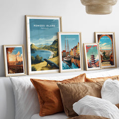 Five framed travel posters of Komodo Island, Copenhagen, Paris, Tokyo, and Barcelona above a bed.