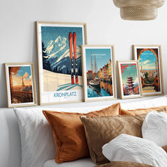 Set of five travel poster art prints in natural wood frames displayed above a bed.