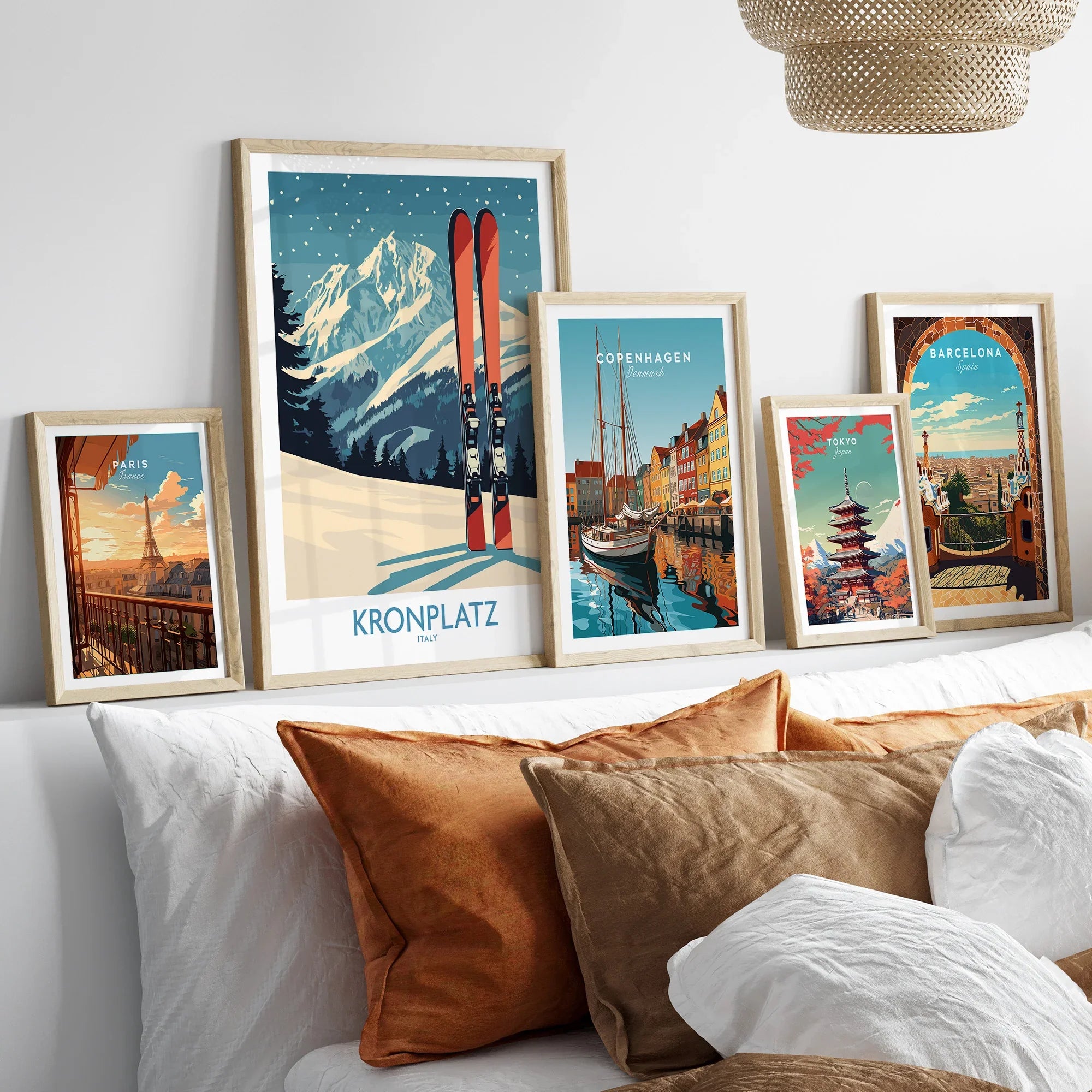 Set of five travel poster art prints in natural wood frames displayed above a bed.