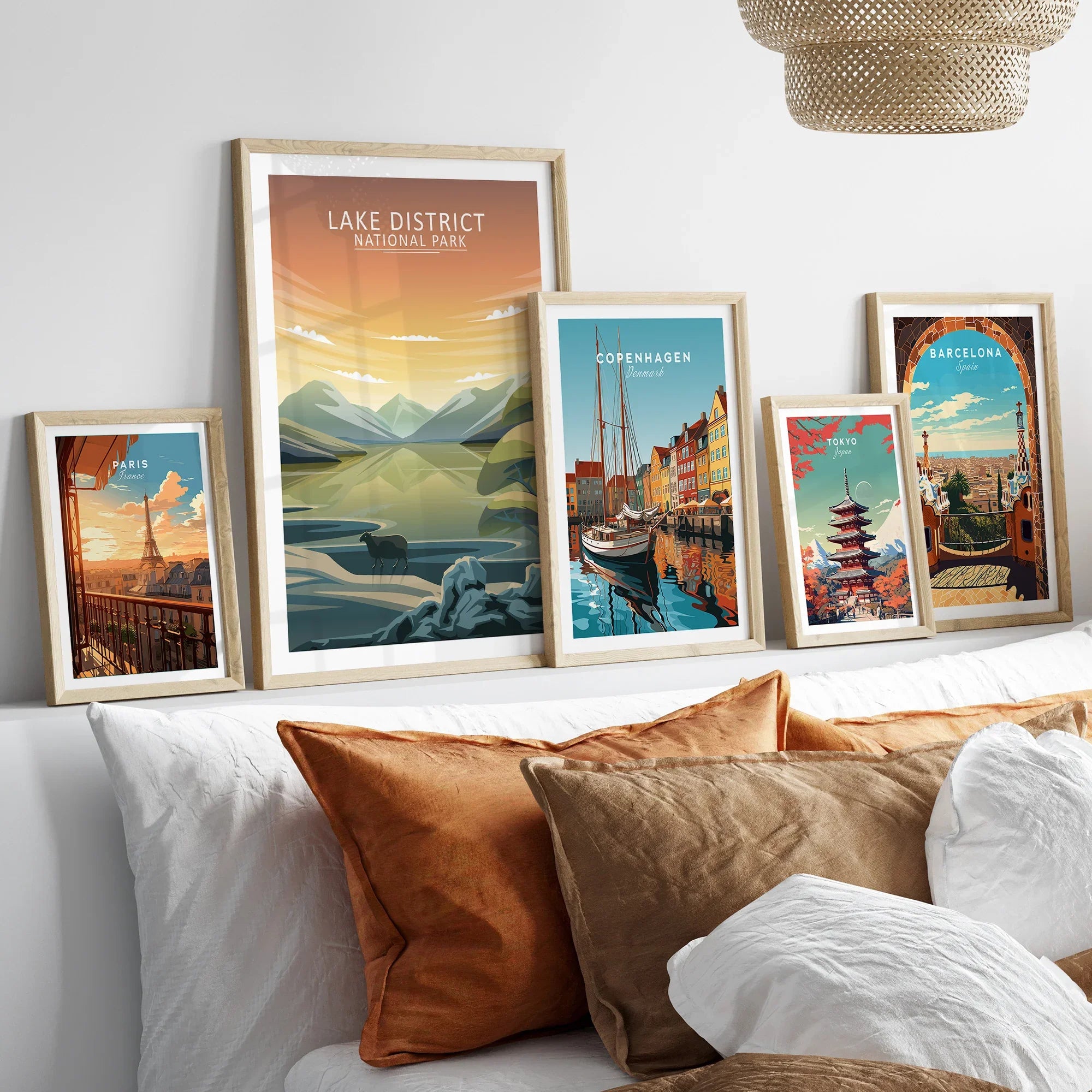Set of five framed travel art prints featuring Paris, Lake District, Copenhagen, Tokyo, and Barcelona above a bed with natural wood frames.