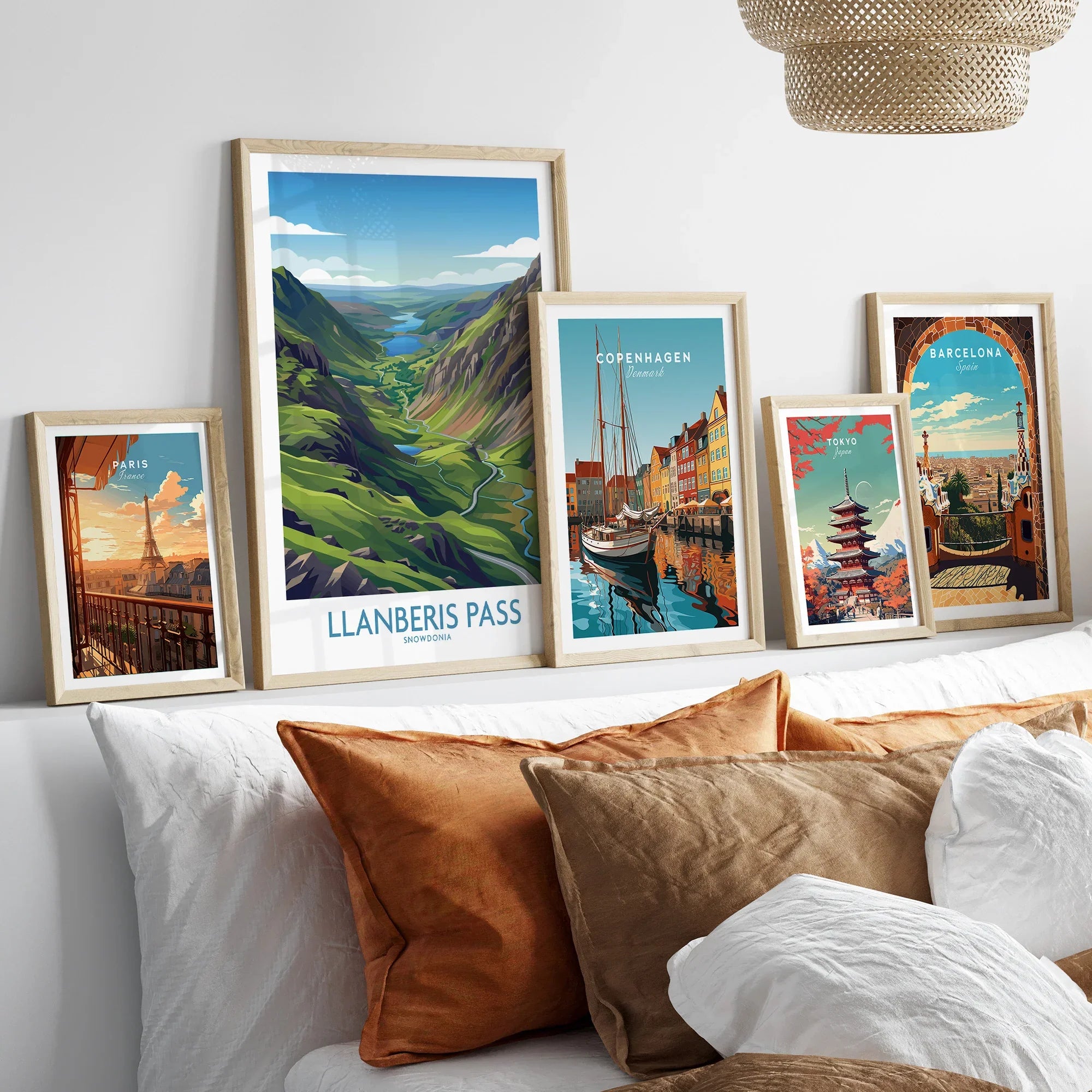 Set of five framed travel posters above bed, featuring Paris, Llanberis Pass, Copenhagen, Tokyo, and Barcelona.