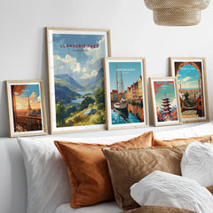 Set of five framed travel art prints featuring Paris, Snowdonia, Copenhagen, Tokyo, and Barcelona above a modern bed with earth-toned pillows.