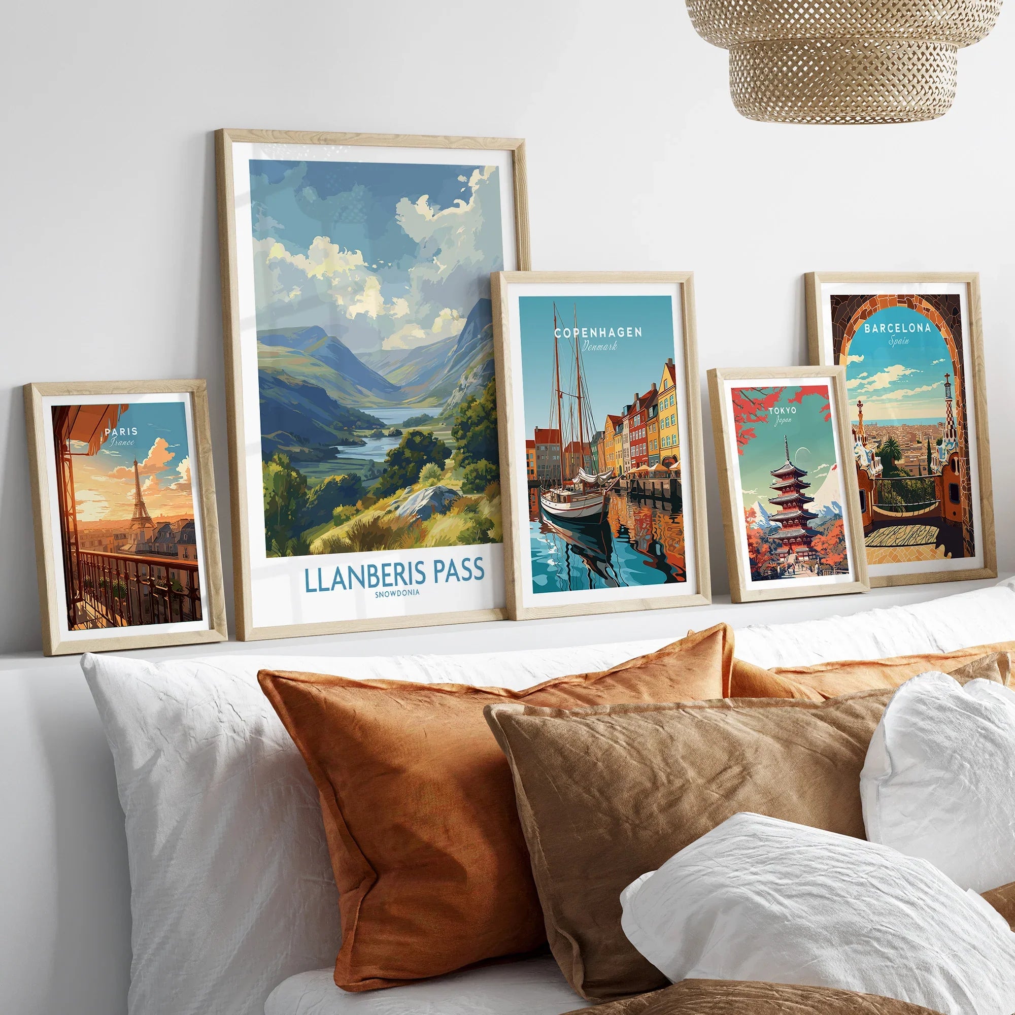 Framed travel art prints of Paris, Snowdonia, Copenhagen, Tokyo, and Barcelona above a bed.