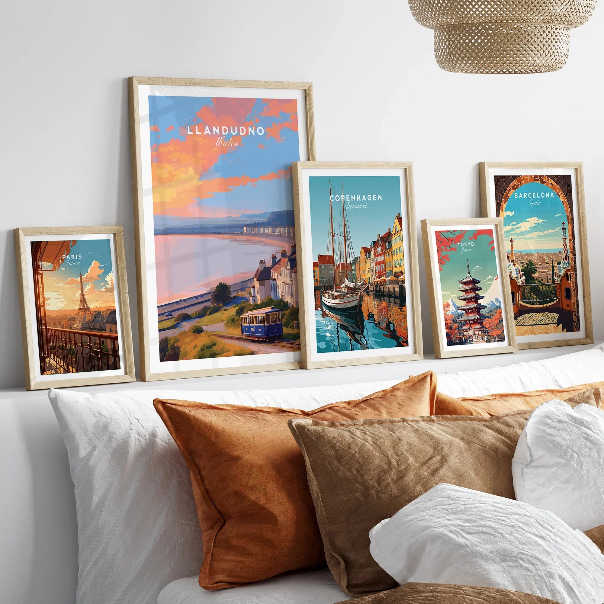 Set of five framed travel art prints above a bed, featuring Paris, Llandudno, Copenhagen, Tokyo, and Barcelona.