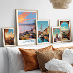 Set of five framed travel art prints above a bed, featuring landmarks from Paris, Llandudno, Copenhagen, Tokyo, and Barcelona in natural wood frames, perfect for wall decor.