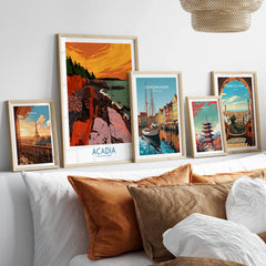 Set of five framed travel posters above a bed, featuring Acadia National Park, Paris, Copenhagen, Tokyo, and Barcelona.