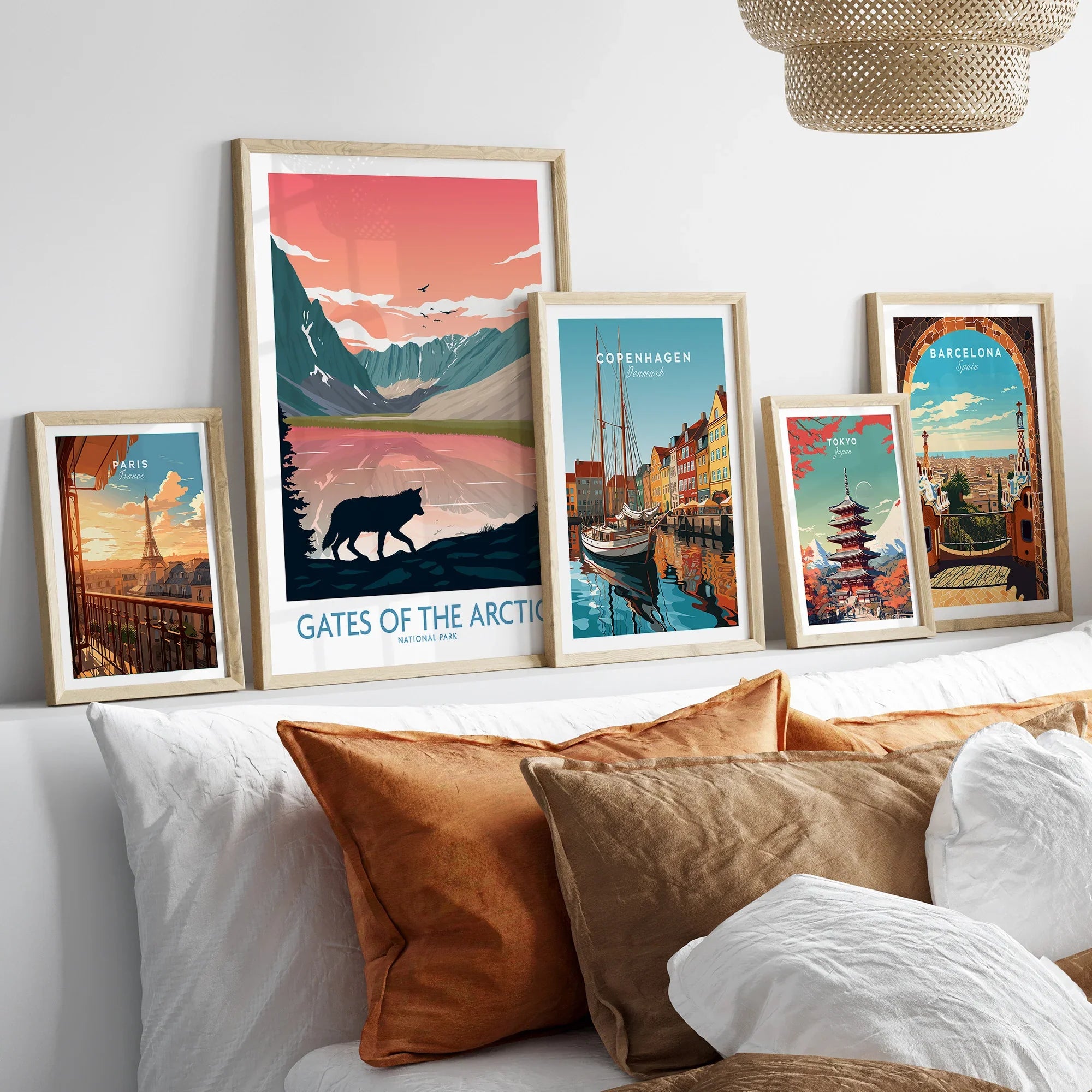 Set of five framed travel art prints above a bed, featuring Paris, Arctic National Park, Copenhagen, Tokyo, and Barcelona scenes.