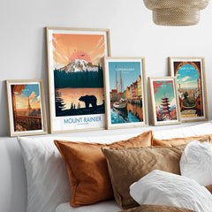 Framed travel and city wall art prints featuring Mount Rainier, Paris, Copenhagen, Tokyo, and Barcelona above a bed.