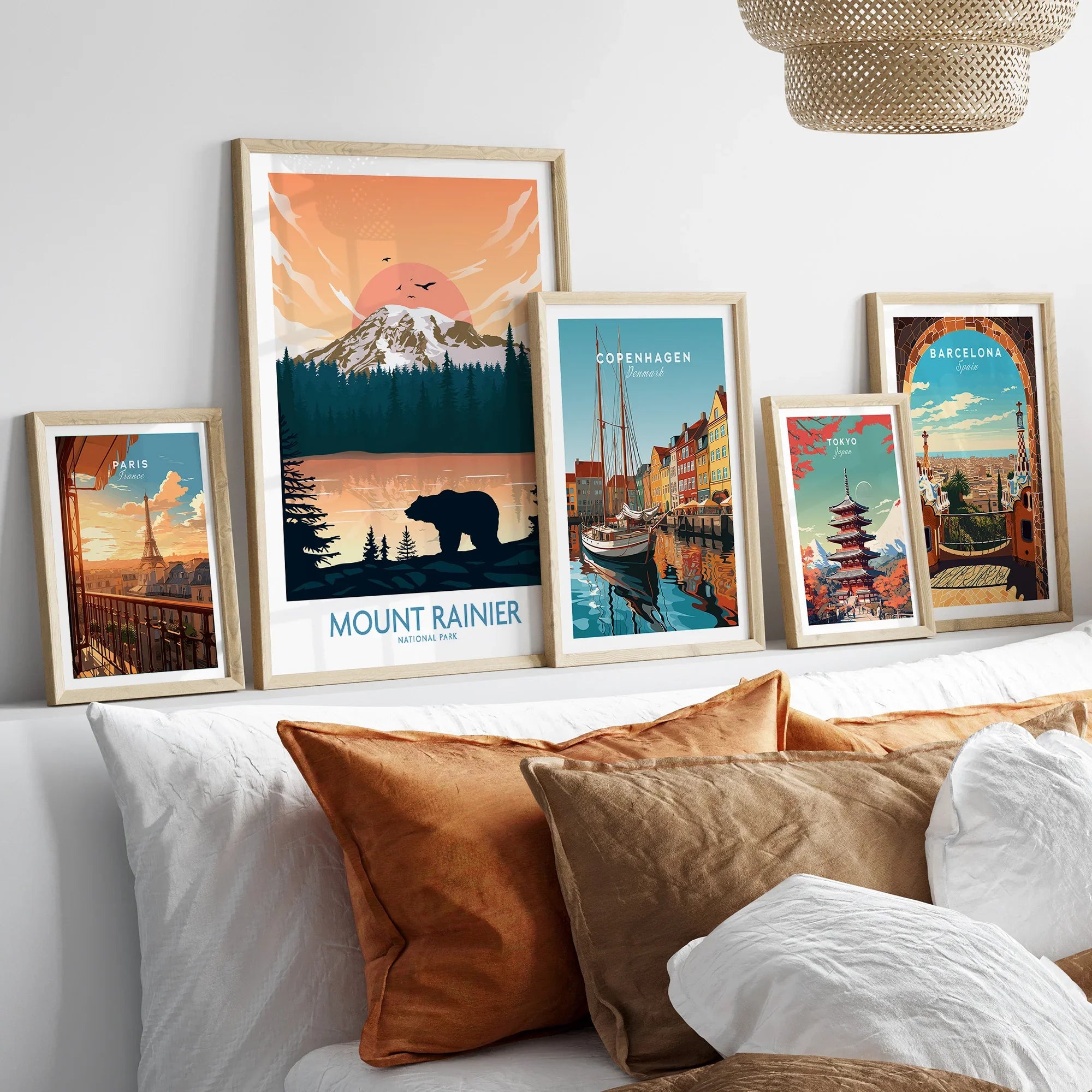 Framed travel and city wall art prints featuring Mount Rainier, Paris, Copenhagen, Tokyo, and Barcelona above a bed.