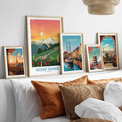Travel poster wall art set in natural wood frames above bed, featuring Mount Rainier, Paris, Copenhagen, Tokyo, and Barcelona prints.