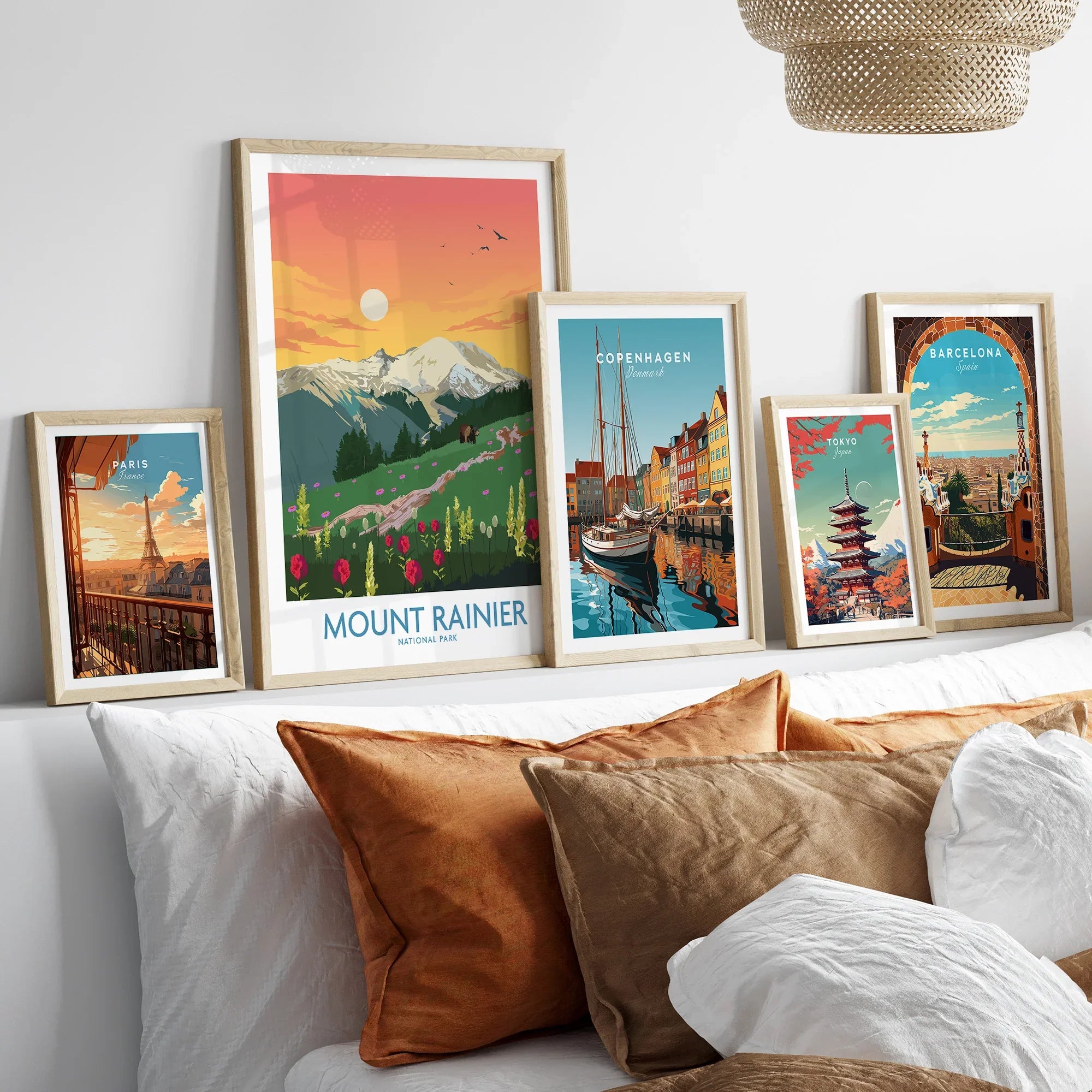 Travel poster wall art set in natural wood frames above bed, featuring Mount Rainier, Paris, Copenhagen, Tokyo, and Barcelona prints.