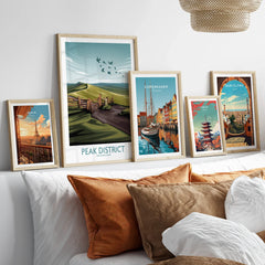 Set of five framed travel art prints with city and nature scenes above a bed with brown pillows.