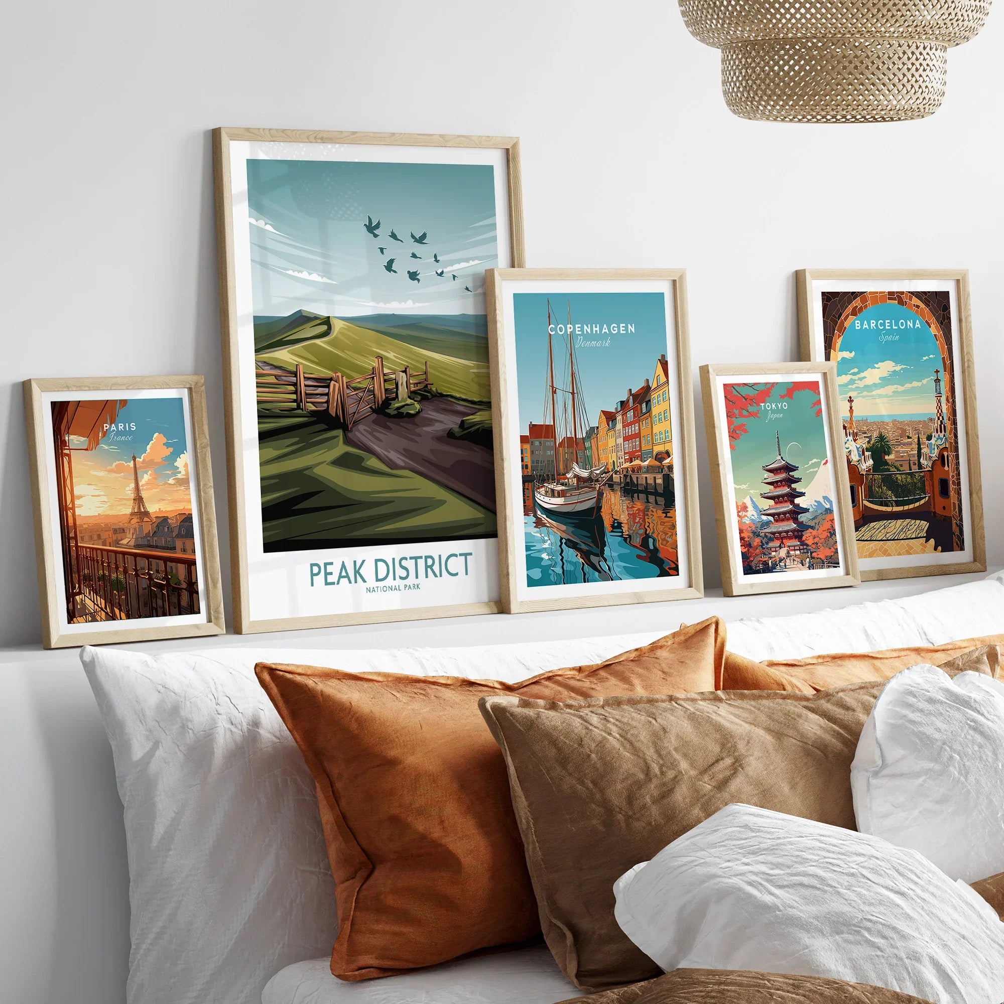 Set of five framed travel art prints with city and nature scenes above a bed with brown pillows.
