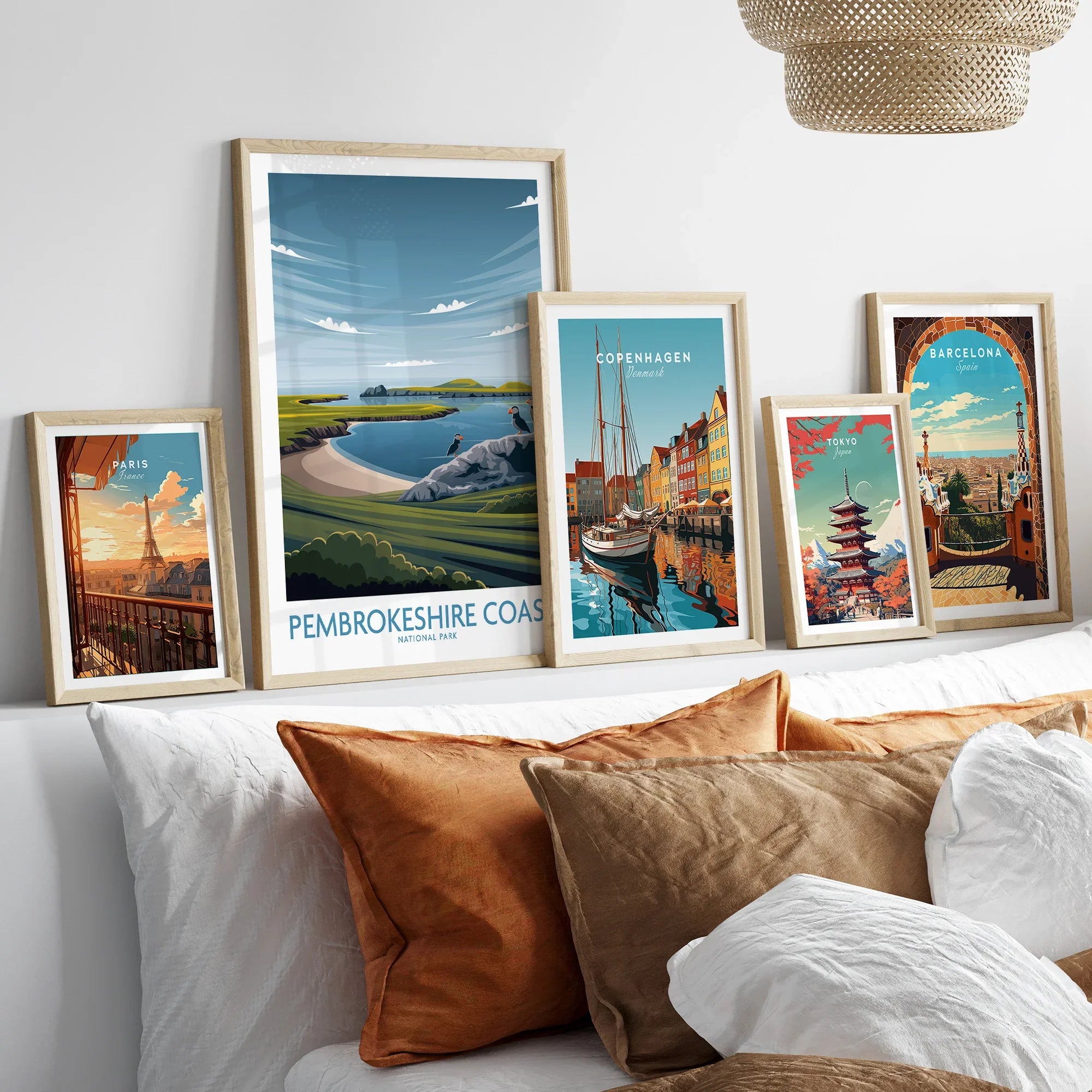 Framed travel posters of Paris, Pembrokeshire Coast, Copenhagen, Tokyo, and Barcelona above a bed.