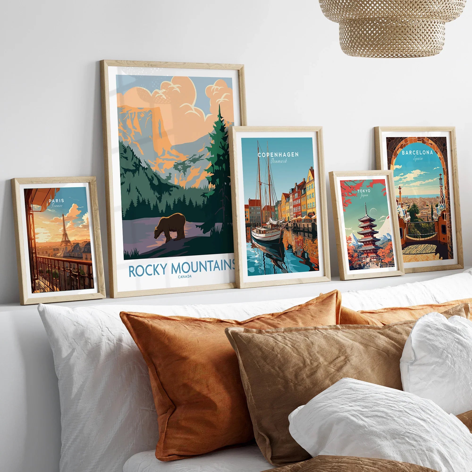 Framed travel posters of Paris, Rocky Mountains, Copenhagen, Tokyo, and Barcelona above a bed.