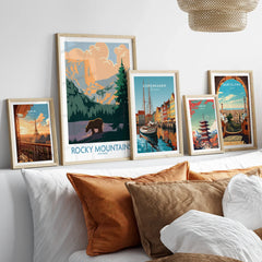 Set of five travel art prints with natural wood frames above bed, featuring city skylines and landscapes.